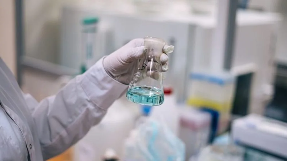 Gloved hand holding a flask of solution in a laboratory
